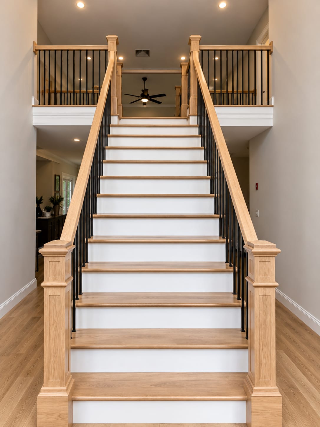 Straight flight of stairs with white oak treads, white risers, black iron balusters and square oak newel posts, seen head on from the bottom