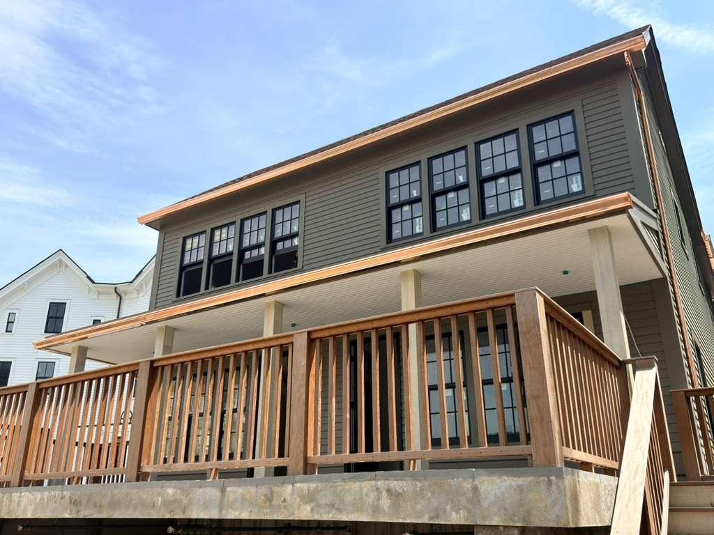 Copper gutter running the full roofline of a grey clapboard house and along the porch below, over a wooden deck rail