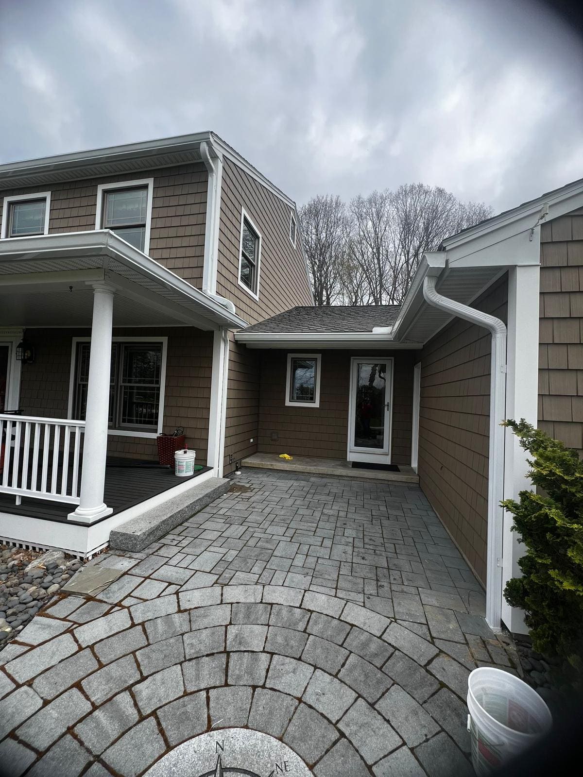 White downspout beside a covered entry, discharging clear of the paver courtyard