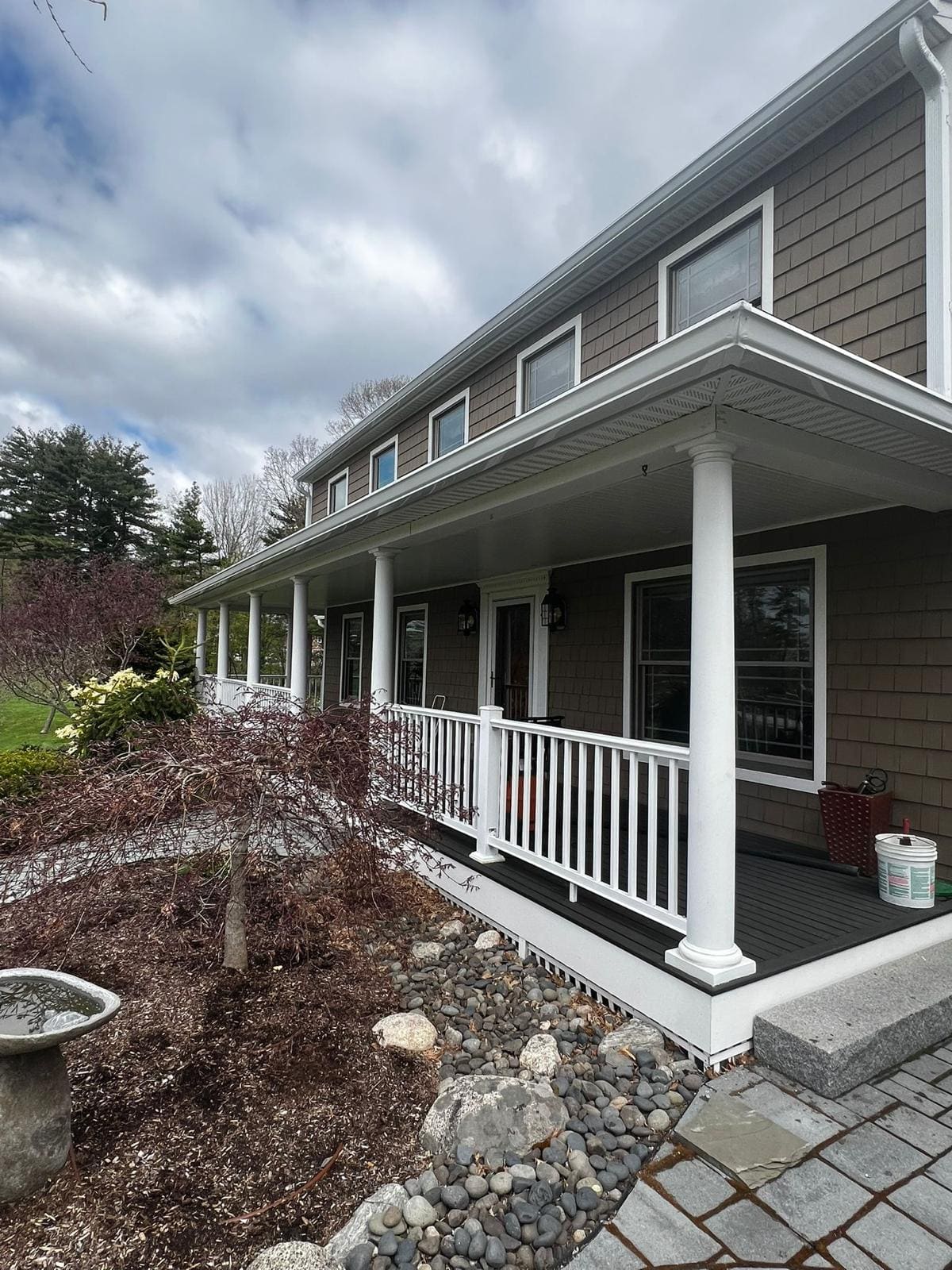Gutter and white downspout along a deep covered porch with square columns
