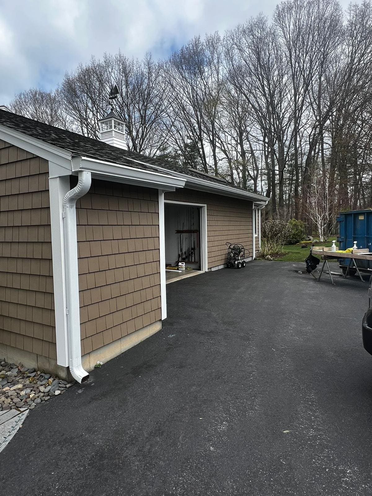 Downspout and elbow carrying water down a shingled garage wall to the driveway
