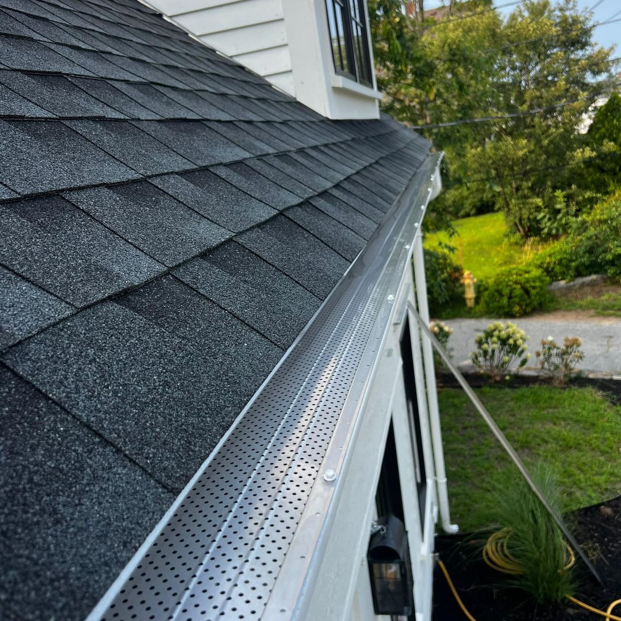 Perforated leaf guard fitted the length of a gutter along an asphalt shingle roof edge
