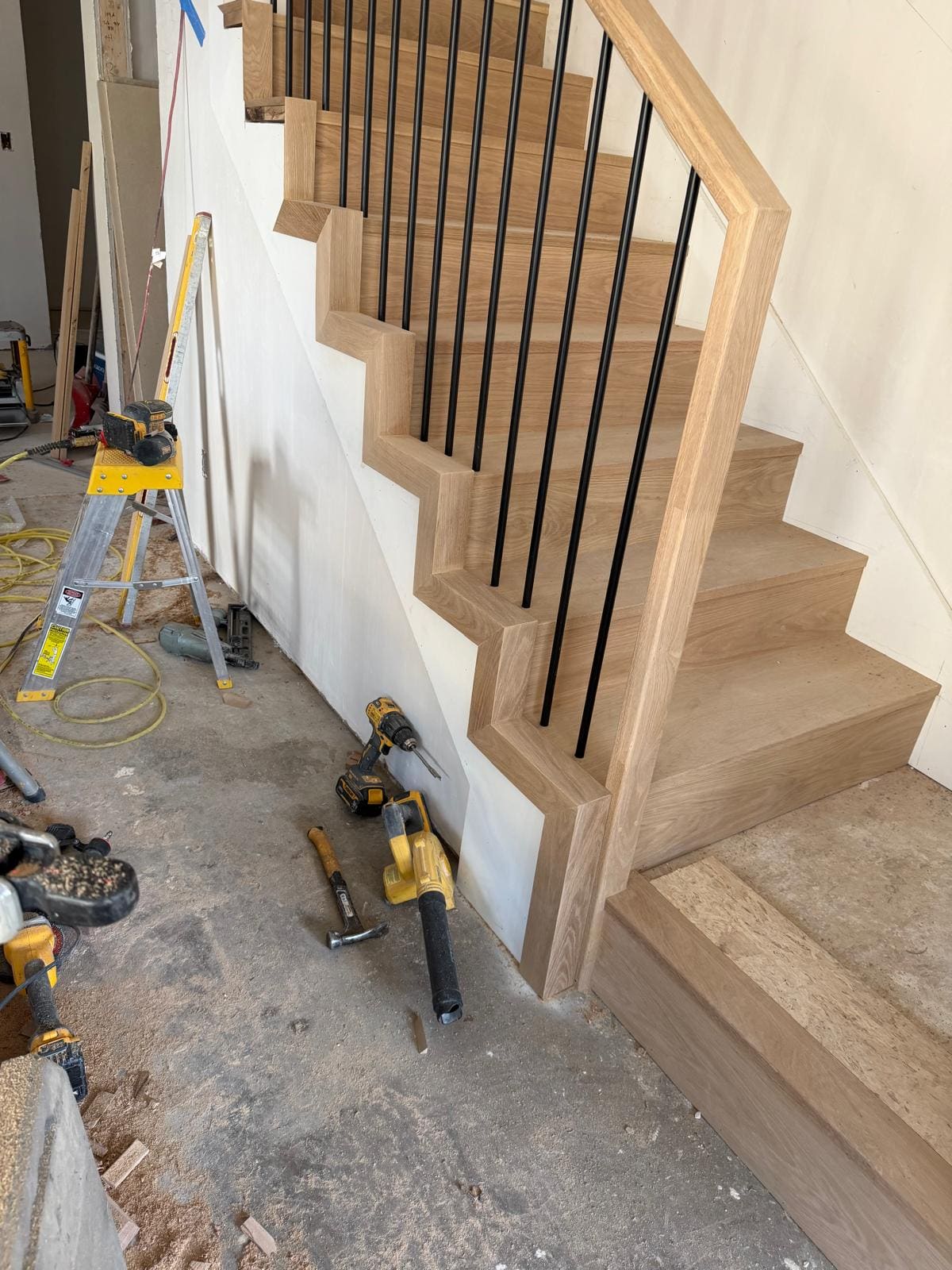 The open side of the staircase, oak rail and black balusters over white risers